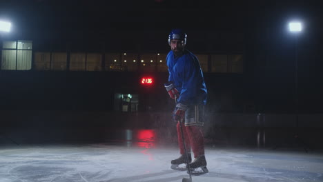 Man-hockey-player-in-hockey-uniform-leaves-with-a-stick-in-his-hands-out-of-the-darkness-and-looks-straight-into-the-camera